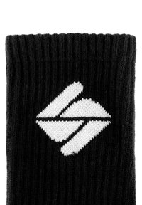 Schwarze gestrickte Socke mit gerippter Textur und einem auffälligen weißen geometrischen Logodesign.