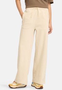 Brede beige broek van zachte stof, met een elastische tailleband met trekkoord en zijzakken. Gestyled met kleurrijke sneakers.