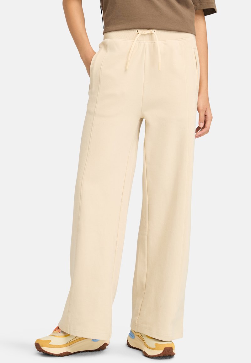 Brede beige broek van zachte stof, met een elastische tailleband met trekkoord en zijzakken. Gestyled met kleurrijke sneakers.