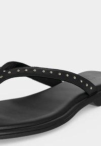 Μαύρο επίπεδο σανδάλι με λεπτά δερμάτινα λουράκια που διαθέτουν μικρές ασημένιες καρφίτσες και ελαφρώς ανυψωμένη φτέρνα.