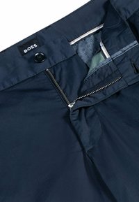 Navy blue trousers featuring a front button, zipper fly, and a smooth, lightweight fabric with a subtle sheen. Inside waistband is lined.