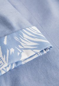 Modrá tkanina s hladkým povrchem má bílo-světle modrý listový vzor na manžetě, která je pečlivě složená.