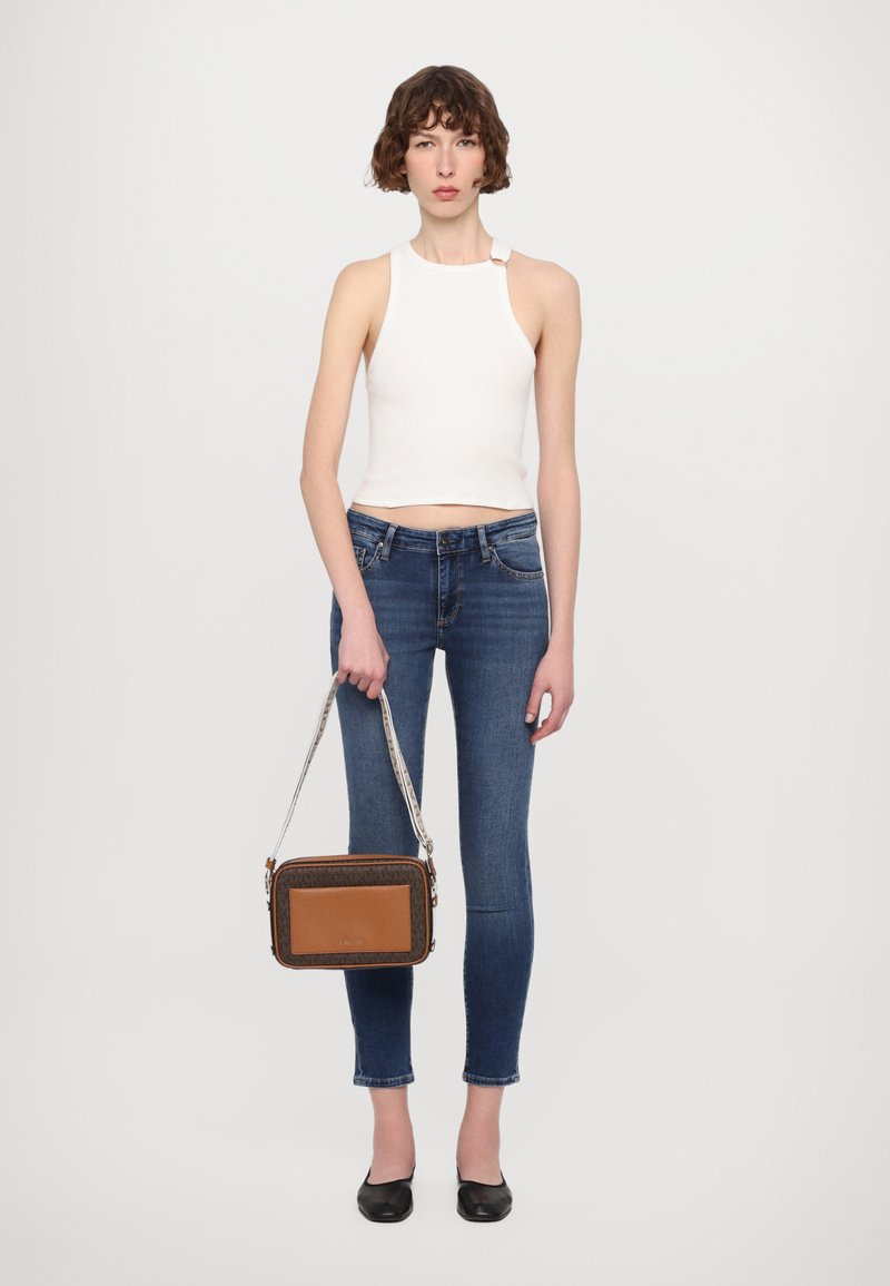Borsa a tracolla marrone e a fantasia con pannello frontale liscio, hardware in argento e tracolla staccabile, indossata da un modello con jeans aderenti.