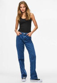 Blue denim jeans with a relaxed fit, five-pocket design, and a button-fly closure, paired with a black tank top and low-top sneakers.