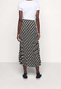 Schwarze Midirock mit einem diamantförmigen Muster in Weiß und Olivgrün. Kombiniert mit einem weißen T-Shirt und schwarzen High-Top-Sneakers.