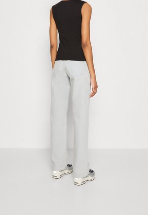 Black sleeveless top paired with light gray wide-leg jeans. The jeans have a subtle texture and visible back pockets, worn with chunky sneakers.
