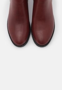 Brązowe skórzane botki za kostkę o gładkim wykończeniu, z okrągłymi czubkami i czarnymi gumowymi podeszwami. Brak widocznych elementów metalowych lub wzorów.