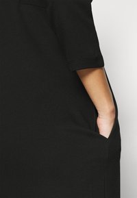 Czarna sukienka o luźnym kroju, z krótkimi podwiniętymi rękawami i bocznymi kieszeniami. Miękka tekstura i gładki materiał z minimalną ilością szwów dla czystego designu.