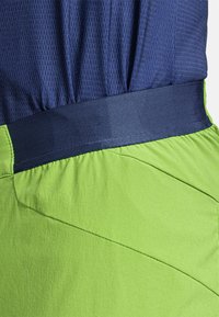 Navy ja kirkasvihreä urheiluvaatetus sisältää teksturoituneen pääosion ja sileän, kiinteän vyötärön, jossa on terävät saumaerottelut alemmassa osassa.