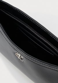 Μαύρη δερμάτινη τσάντα χειρός με λεία υφή, ασημένια αξεσουάρ και κλείσιμο με φερμουάρ. Διαθέτει εσωτερικές θήκες για κάρτες και ανάγλυφο λογότυπο.