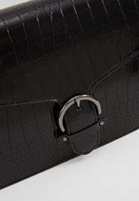 Clutch in pelle nera con effetto coccodrillo, dalla finitura lucida, dotata di una chiusura con fibbia argentata e dettagli di cucitura lungo i bordi.