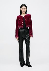 Jachetă scurtă din catifea fucsia, cu tiv cu franjuri și detalii la buzunare, asortată cu pantaloni negri din piele cu ținte pe lateral și pantofi cu vârf ascuțit.