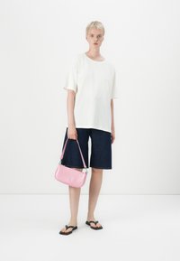 Hvid kortærmet skjorte, mørk denim Bermuda shorts og sorte flip-flops. Holder en pink håndtaske med krokodilleskind-tekstur og sølvhardware.