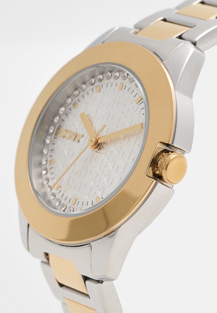 Montre en métal au design bicolore argent et or, avec un cadran blanc texturé portant un logo et des pierres accentuées autour de la lunette.