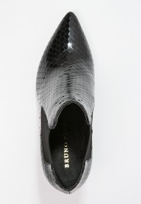 Zapato negro, texturizado, con puntera afilada, que presenta un patrón de serpiente y paneles laterales elásticos. El interior tiene una marca dorada.