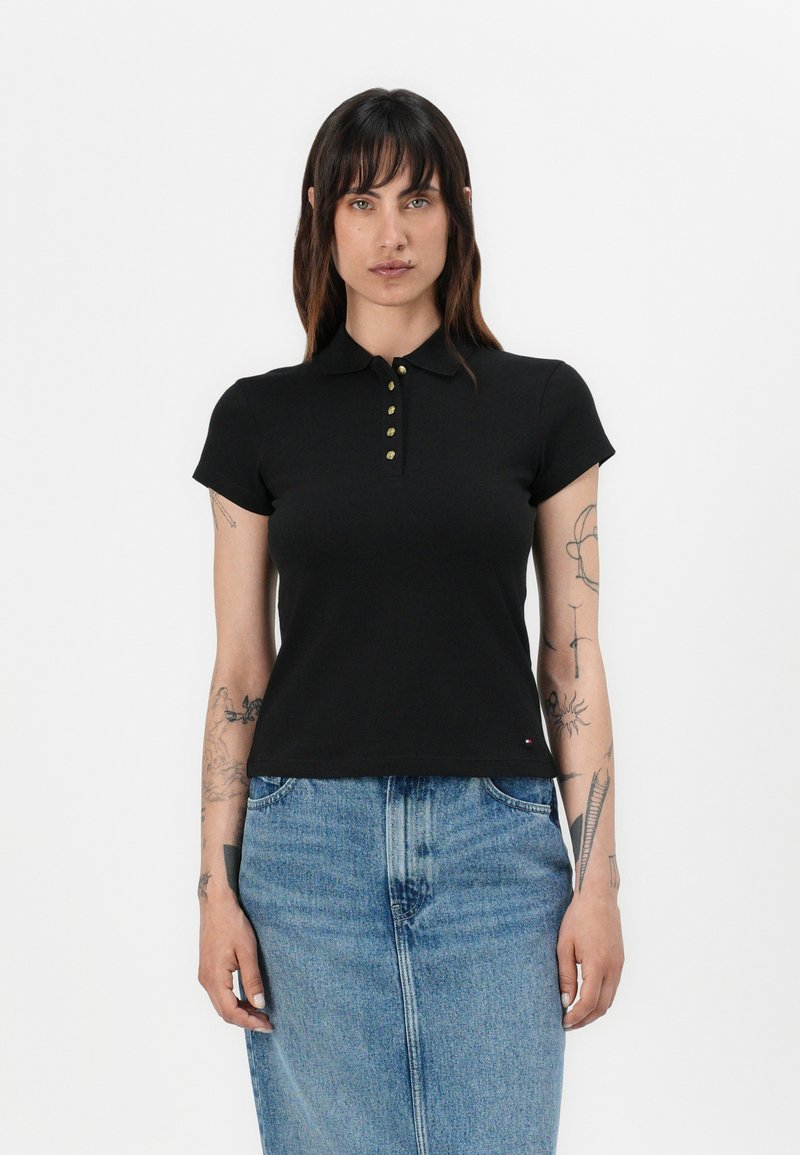 Zwarte poloshirt met korte mouwen en een kraag, afgewerkt met goudkleurige knopen. Gecombineerd met een lichtblauwe spijkerrok.