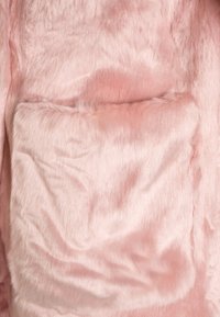 Tela de pelo sintético rosa con una textura suave, que presenta un gran bolsillo blando integrado en el diseño. Se puede apreciar un ligero brillo lustroso.