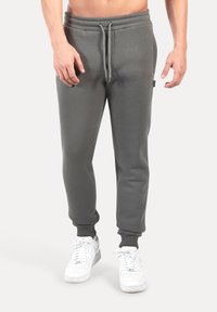 Pantalones deportivos grises con cinturilla y puños elásticos, hechos de un material suave. Combinados con zapatillas blancas y una discreta etiqueta de marca en el lateral.