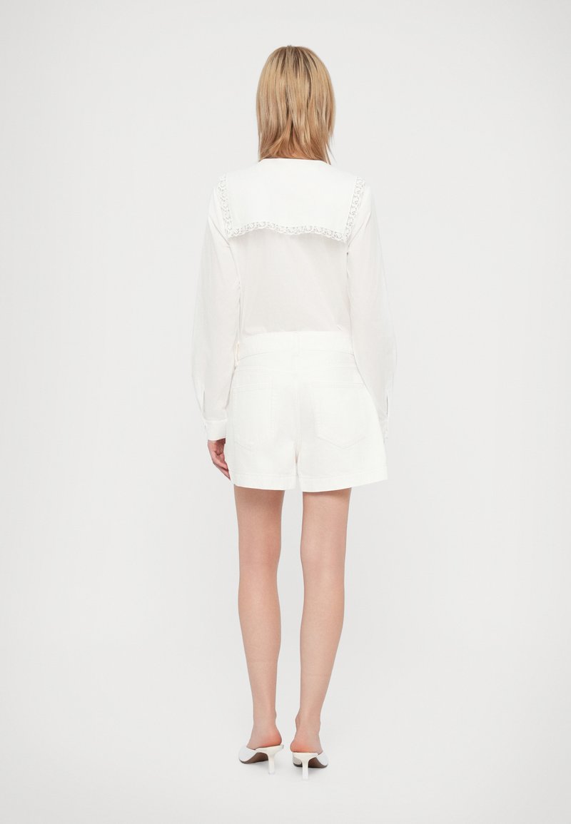 Blouse blanche avec un col en dentelle, associée à un short en denim blanc. Design simple, tissu léger et coupe courte avec poches.