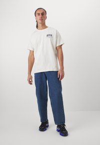 Hvit bomull T-skjorte med "INTER" grafikk, kombinert med blå denimjeans og svarte joggesko med blå detaljer.
