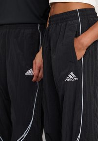 Sorte, lette joggebukser med teksturert stoff, med elastisk midje, sidelommer og hvite aksentstriper. Adidas-logo vist.
