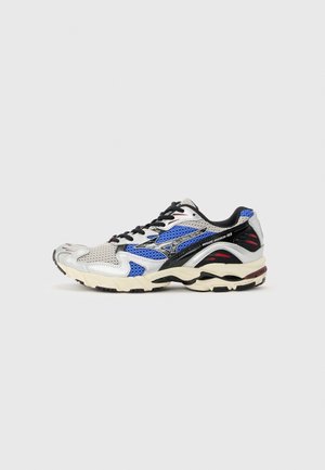 Scarpa da corsa con pannelli in mesh e sintetico bianchi, blu, neri e rossi, lacci neri e suola imbottita beige su sfondo grigio chiaro.