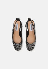 Musta slingback-kengät, joissa on hopeiset niitit, pyöreä kärki ja sileä sisus mukavuutta varten. Litteä korko vakauden takia.