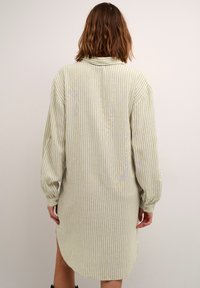 Chemise longue rayée verte et blanche avec col, épaules tombantes et coupe ample. Présente des poignets boutonnés et un ourlet arrondi.