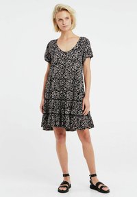 Schwarzes Blumenkleid mit V-Ausschnitt, kurzen Ärmeln, Rüschensaum und Knopfdetails. Hat ein Muster aus hellen Blättern auf dunklem Hintergrund.