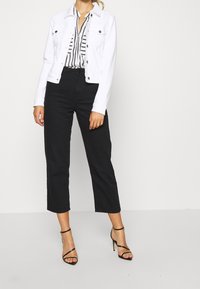 Giubbotto di jeans bianco, blusa a righe, pantaloni neri tagliati e tacchi a strappo neri. Le caratteristiche includono bottoni, tasche e una vestibilità rilassata.