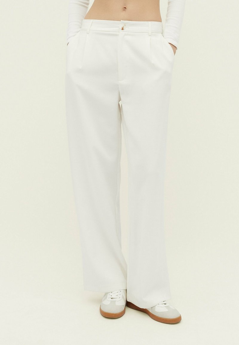 Pantalon blanc taille haute à jambes larges avec poches latérales, porté avec des baskets blanches et un top court à manches longues.