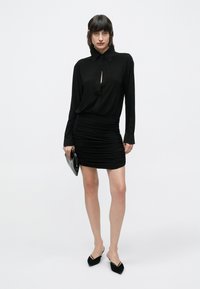 Μαύρο φόρεμα με μακριά μανίκια, άνοιγμα στο μπροστινό μέρος σε σχήμα κλειδαρότρυπας και ραβδώσεις στη φούστα. Συνδυασμένο με μαύρο clutch και μυτερά φλατ παπούτσια.