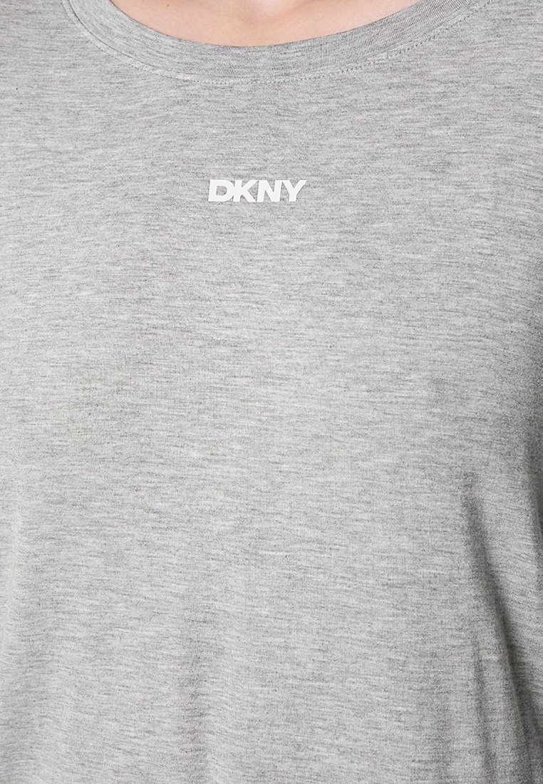 Szary t-shirt z okrągłym dekoltem z białym logo DKNY umieszczonym centrycznie przy kołnierzyku, noszony przez osobę widoczną od szyi do połowy klatki piersiowej.