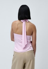 Lys rosa halterneck topp med en sløyfedetalj bak, laget av mykt stoff. Kombinert med beige bukser, med et enkelt design.