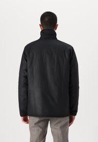 Jachetă waterproof neagră cu guler înalt, având o textură netedă și un design minimalist. Vederea din spate evidențiază linii simple și curate.