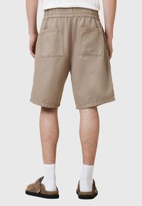 Beiga shorts med elastisk midja, två bakfickor och lös passform. Bärs med vita strumpor och bruna slip-on skor.