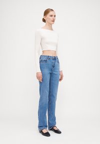 Bela kratka majica z dolgimi rokavi, modri ravni jeans s žepi in črne ravne čevlje. Gladek material in običajna tekstura jeansa.