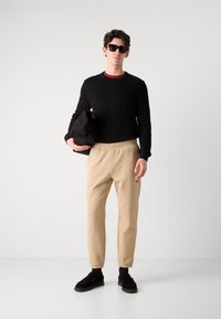 Čierny rebrovaný dlhý rukáv, béžové elastické nohavice, čierne tenisky, nesúci čiernu tašku, nosí tmavé slnečné okuliare. Jednoduchý, neformálny outfit.