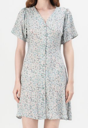 Mujer con un vestido azul claro de manga corta con estampado floral pequeño en blanco y rojo, y cierre frontal con botones.