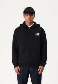 Hanorac negru cu fermoar, cu buzunare frontale, glugă cu șnur și logo-ul alb brodat "HUF" pe pieptul stâng. Material moale, croială casual.