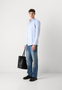 Camisa de rayas azul claro, jeans de mezclilla, zapatos de cuero negros y una bolsa tote negra. El conjunto presenta detalles en los botones y jeans de corte recto.