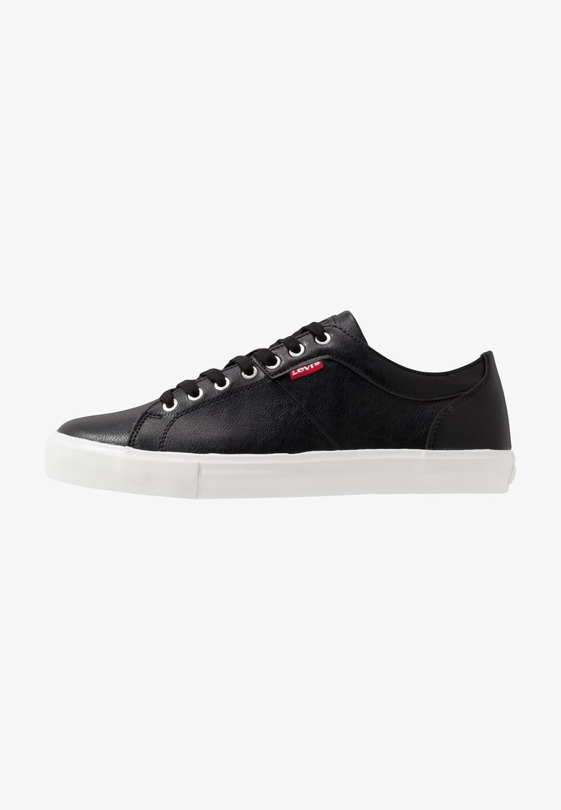 Baskets basses noires Levi's avec semelle en caoutchouc blanche, lacets noirs et étiquette rouge avec le logo Levi's sur le côté.