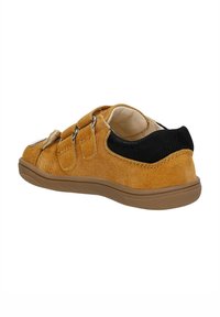 Scarpa in suede tan con due straps in velcro, tessuto nero attorno alla caviglia e suola in gomma. Texture liscia con forma arrotondata.