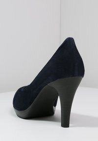 Scarpa con tacco alto in camoscio blu navy, con punta affusolata e una superficie liscia e opaca. Il tacco è sottile e misura circa 10 cm.