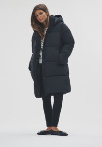 Fekete, kapucnis steppelt télikabát elöl cipzárral. Csíkos felsővel viselve, fekete nadrággal és balerinacipővel párosítva.