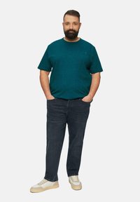 Türkisblaue gepunktete T-Shirt, dunkle Jeans und beige Sneaker. Das T-Shirt hat einen Rundhalsausschnitt, kurze Ärmel und eine lässige Passform.