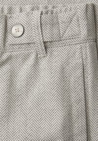 Detailní záběr šedé a bílé rybí kost tkaniny s knoflíkem a smyčkou na pásek z tkaniny na pasu oděvu.