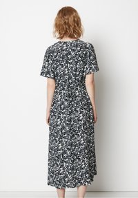 Svartvit blommig mönstrad midiklänning med korta ärmar, resårmidja och en flödande kjol som sträcker sig till mitten av vaden.