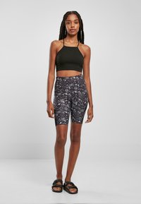 Zwarte cropped tanktop, zwarte en grijze fietsshorts met een patroon van hemelse motieven, en zwarte sandalen. Soepele textuur, strakke pasvorm.