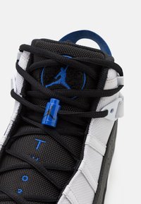 Černobílé sportovní boty s modrými akcenty, síťovinou a syntetickými materiály, výraznými šňůrkami a logem Jumpman na jazyku a zámku šňůrek.